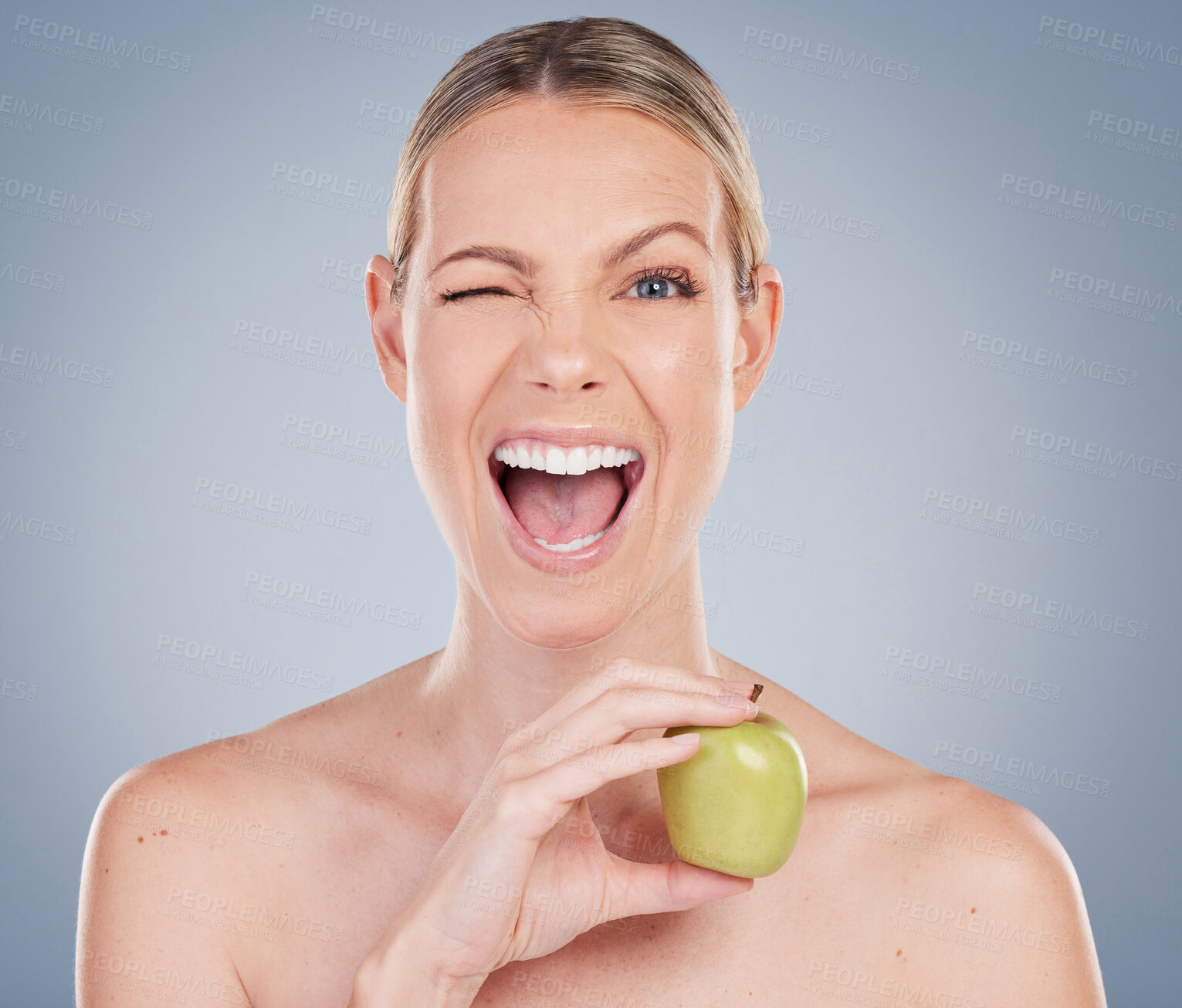 Buy stock photo Studio portrait of an attractive young woman posing with an apple against a grey background