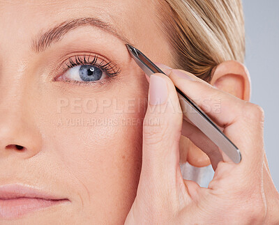 Buy stock photo Studio portrait of an attractive young woman plucking her eyebrows against a grey background