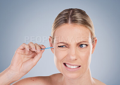 Buy stock photo Girl, cleaning and ear for hygiene in studio for personal self care, grooming and daily routine for wellness or health. Woman, uncomfortable and isolated on grey background with cotton bud for earwax