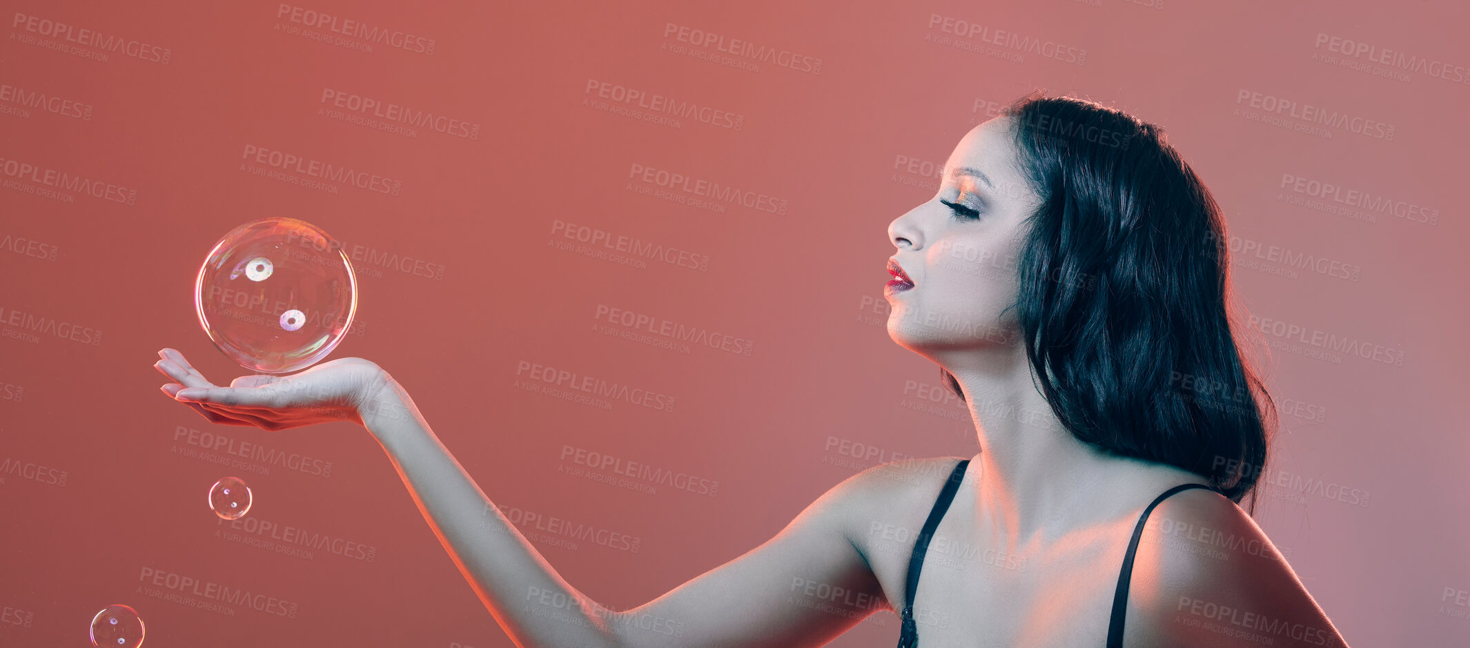 Buy stock photo Cropped shot of a beautiful young woman posing in studio surrounded by bubbles against a red background