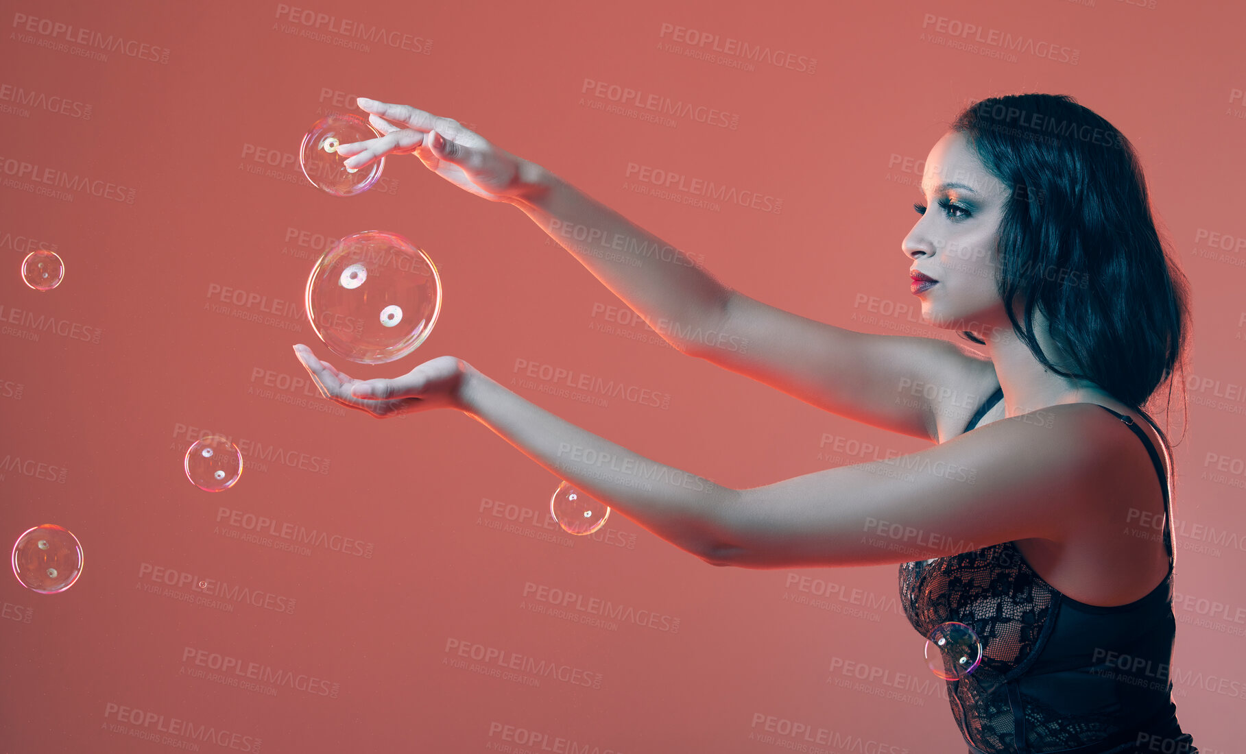 Buy stock photo Cropped shot of a beautiful young woman posing in studio surrounded by bubbles against a red background