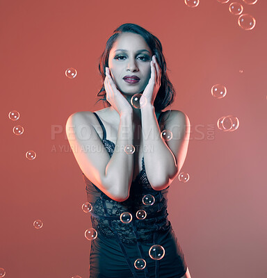 Buy stock photo Cropped portrait of a beautiful young woman posing in studio surrounded by bubbles against a red background