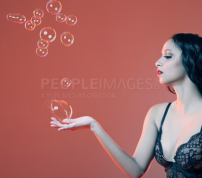 Buy stock photo Cropped shot of a beautiful young woman posing in studio surrounded by bubbles against a red background