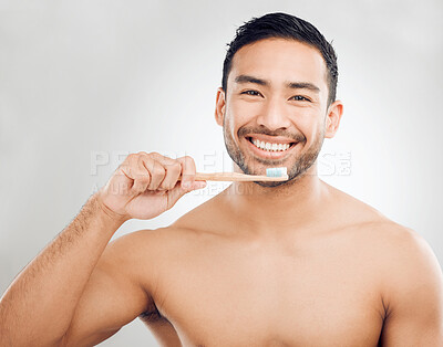 Buy stock photo Portrait, man and brushing teeth for hygiene in studio with oral care and toothpaste with whitening results. Asian guy, dental and bamboo brush with clean mouth for healthy gums by white background