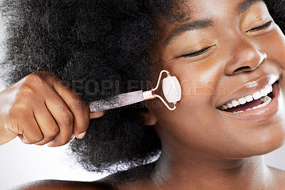 Buy stock photo Studio shot of an attractive young woman using a jade roller on her face against a grey background