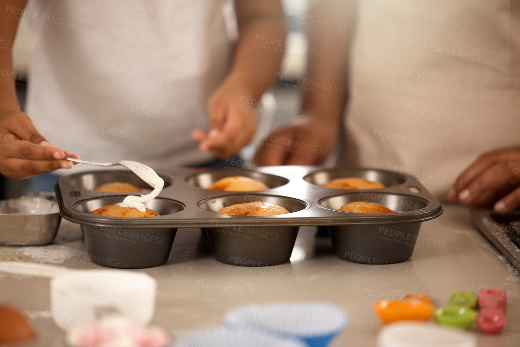 Buy stock photo People, baking and icing cupcakes in home, family fun and spoon with tray on kitchen counter. Child, parent and hands decorating treat on weekend break in apartment, culinary skills and bonding