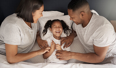 Buy stock photo Shot of a young couple sitting in bed and bonding with their daughter by tickling her