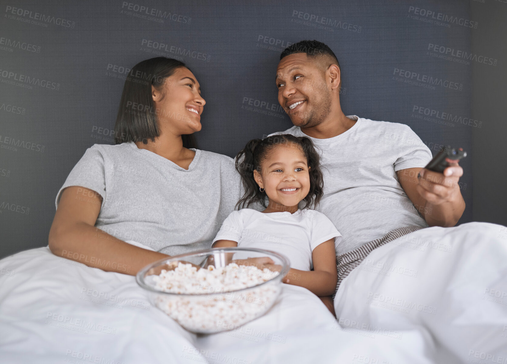 Buy stock photo Shot of a young couple sitting in bed with their daughter and getting ready to watch a movie