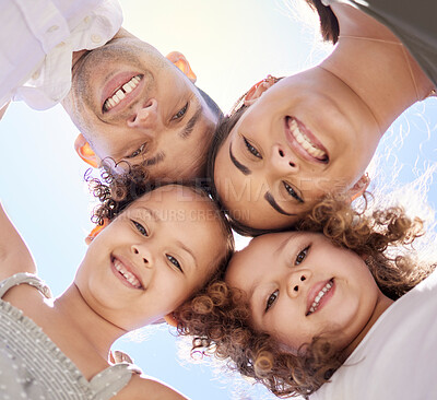 Buy stock photo Low angle portrait of a happy young family huddled together on a fun day outdoors
