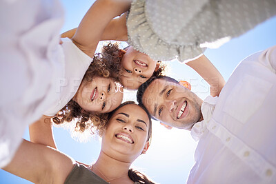 Buy stock photo Low angle portrait of a happy young family huddled together on a fun day outdoors