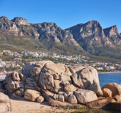 Buy stock photo Beautiful, nature view of the beach front or rocky boulder on the seashore against a mountain landscape and blue sky on a Summer day. Calm scene of the beach and the ocean in the city.