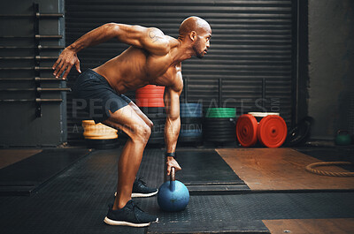 Buy stock photo Shot of a muscular young man exercising with a kettlebell in a gym