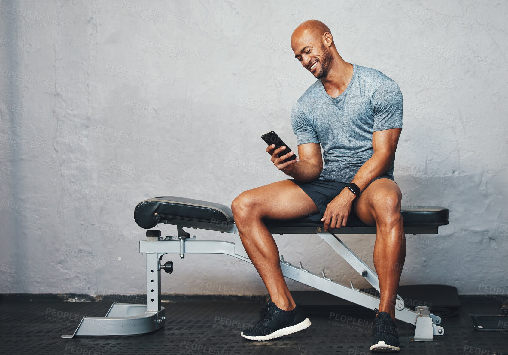 Buy stock photo Shot of a muscular young man using a cellphone in a gym