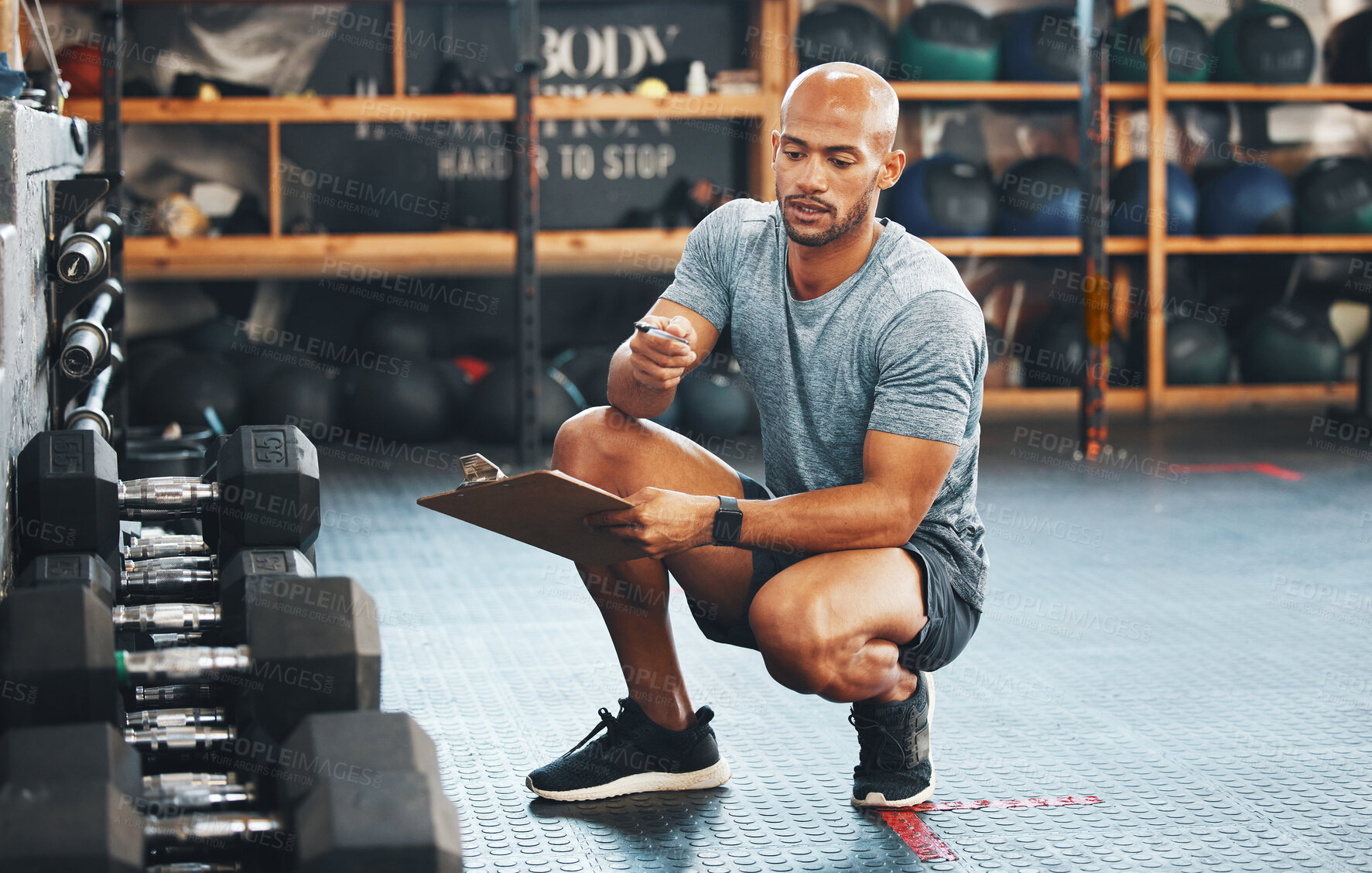 Buy stock photo Shot of a muscular young man using a clipboard while checking equipment in a gym