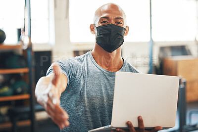 Buy stock photo Portrait of a muscular young man wearing a face mask and extending a handshake while using a laptop in a gym