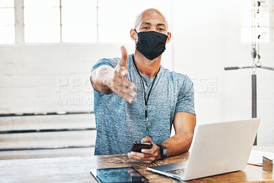 Buy stock photo Portrait of a muscular young man wearing a face mask and extending a handshake while using a laptop in a gym