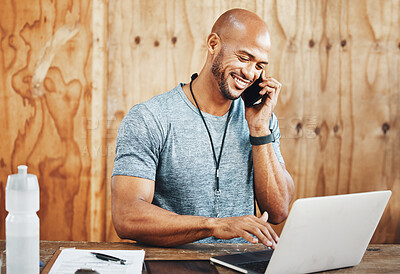 Buy stock photo Shot of a muscular young man talking on a cellphone and using a laptop while working in a gym