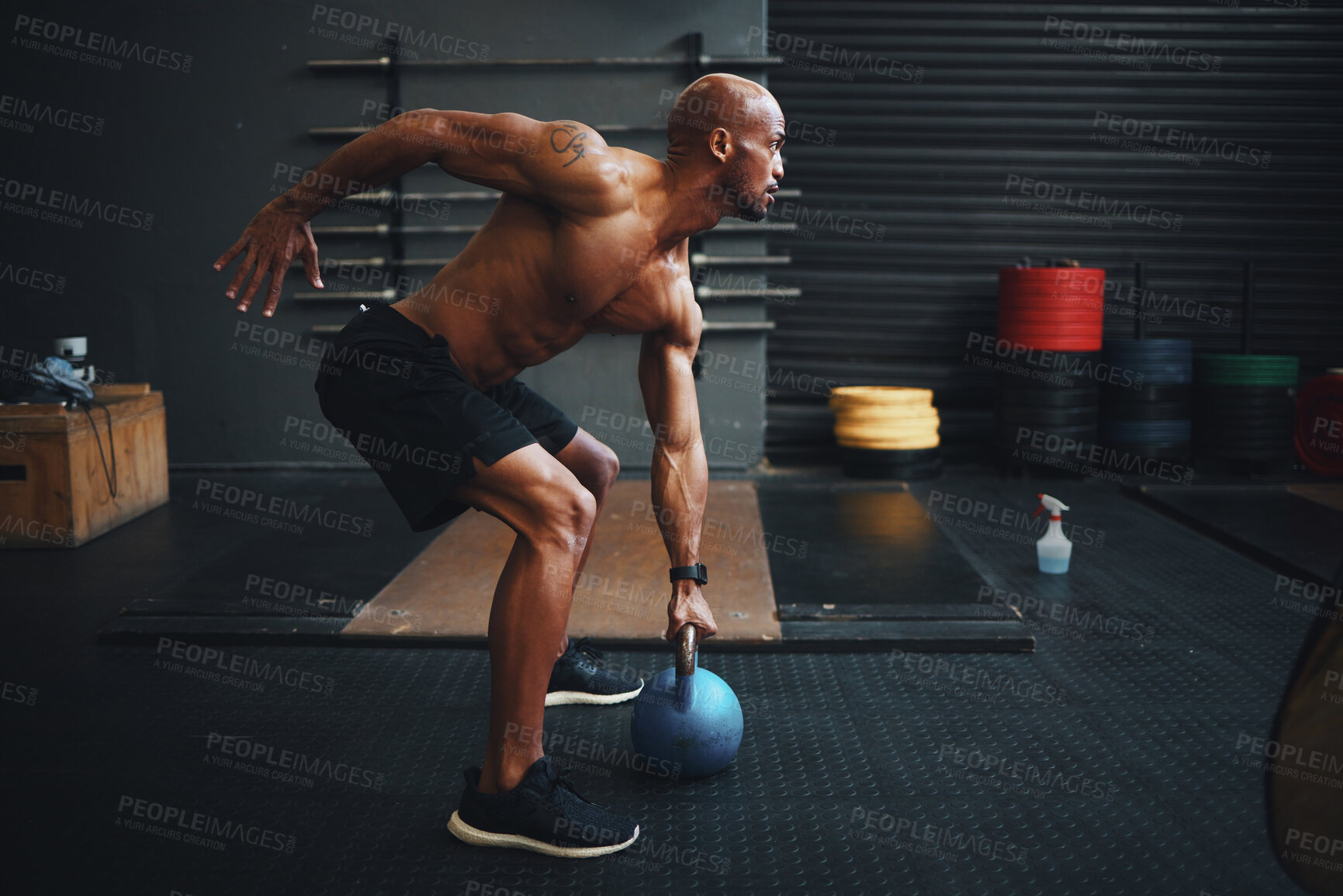 Buy stock photo Shot of a muscular young man exercising with a kettlebell in a gym