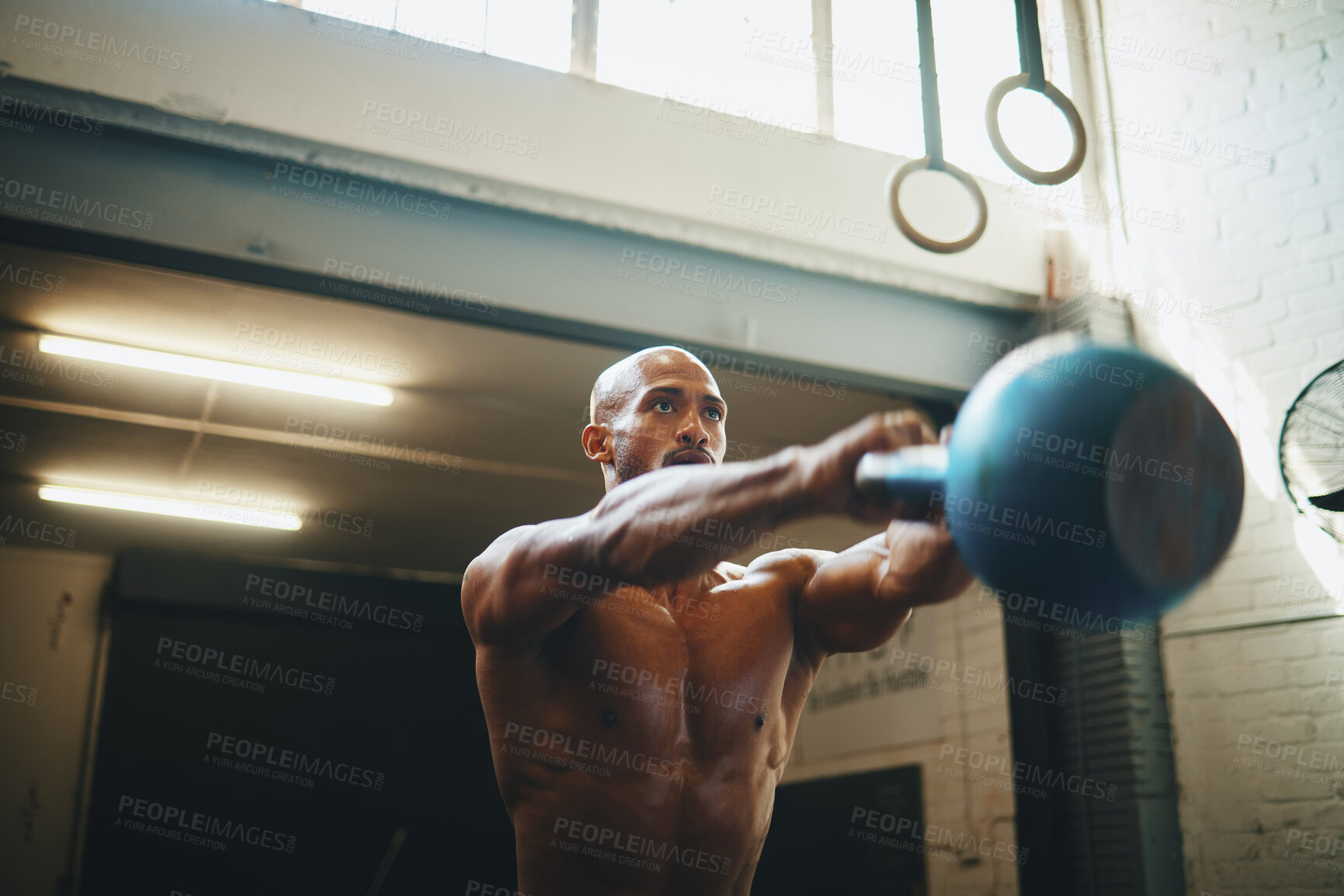 Buy stock photo Low angle shot of a muscular young man exercising with a kettlebell in a gym