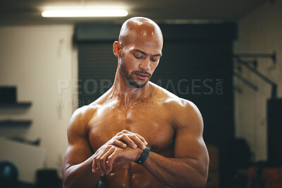 Buy stock photo Shot of a muscular young man checking his watch while exercising in a gym