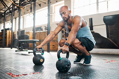 Buy stock photo Shot of a young man getting ready to use kettlebells in his gym