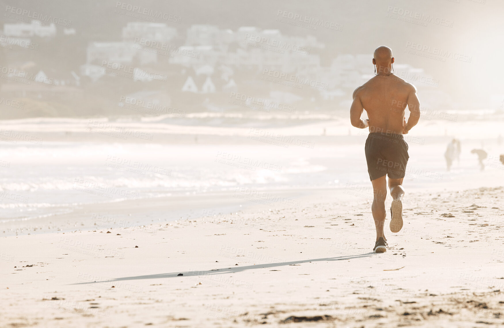 Buy stock photo Back, man and running at ocean for fitness, exercise and wellness at Brazil space. Sports person, active and earphones on beach for endurance workout, marathon preparation and training goal ambition