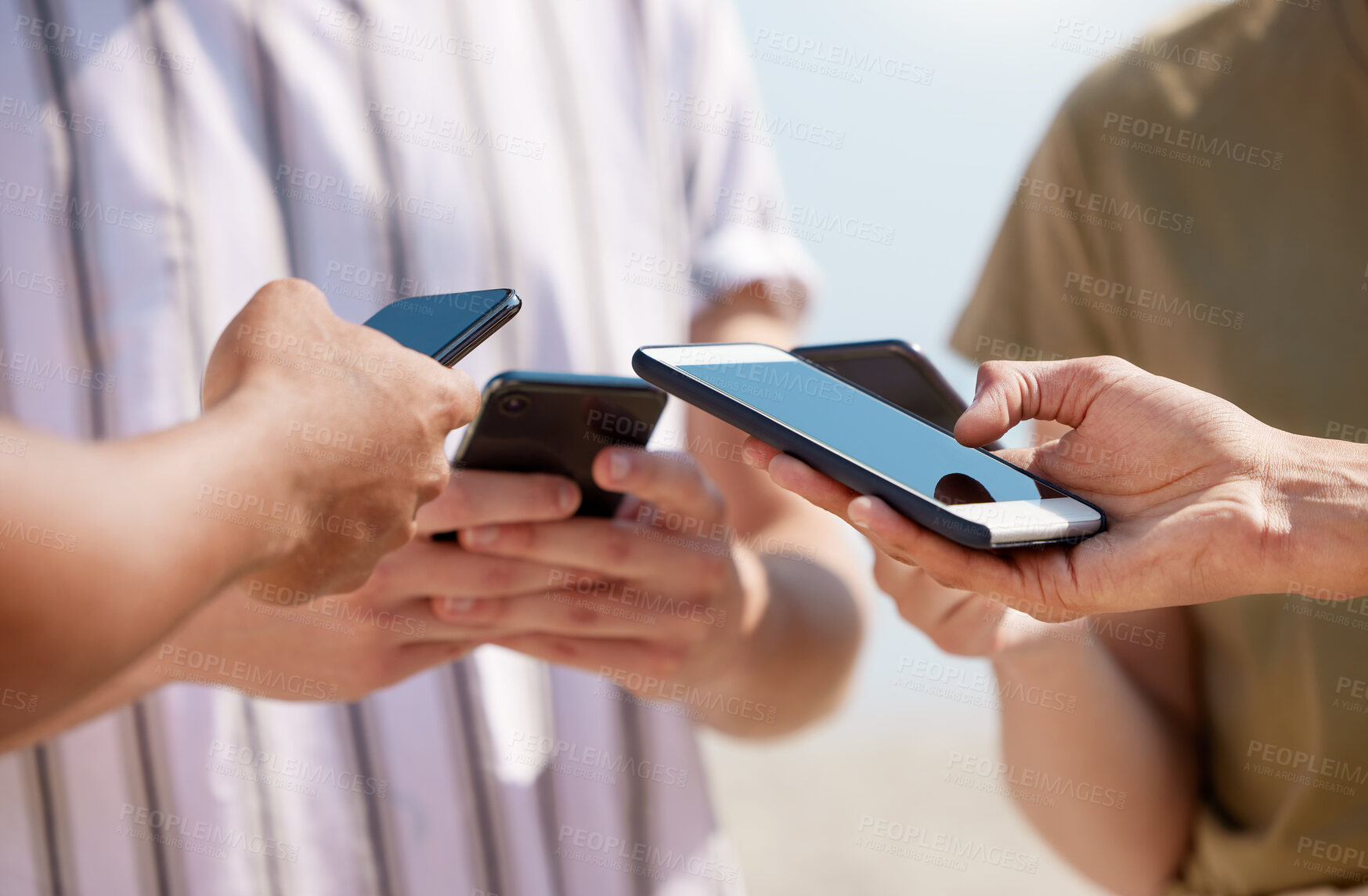 Buy stock photo Shot of a group of unrecognizable friends using their phones outside