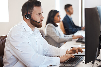 Buy stock photo Shot of a young call centre agent working in an office with his colleague in the background