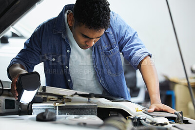 Buy stock photo Shot of a handsome young male mechanic working on the engine of a car during a service