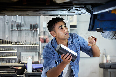 Buy stock photo Shot of a handsome young male mechanic working on the engine of a car during a service