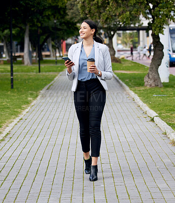 Buy stock photo Shot of a young businesswoman making her way to work while using her smartphone and drinking coffee