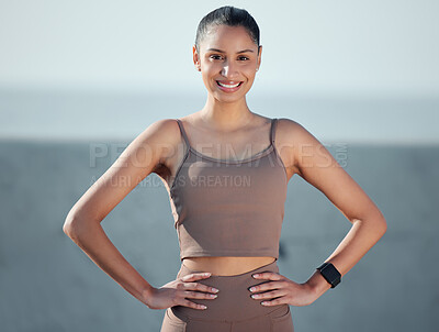 Buy stock photo Portrait of a sporty young woman standing with her hands on her hips while exercising outdoors