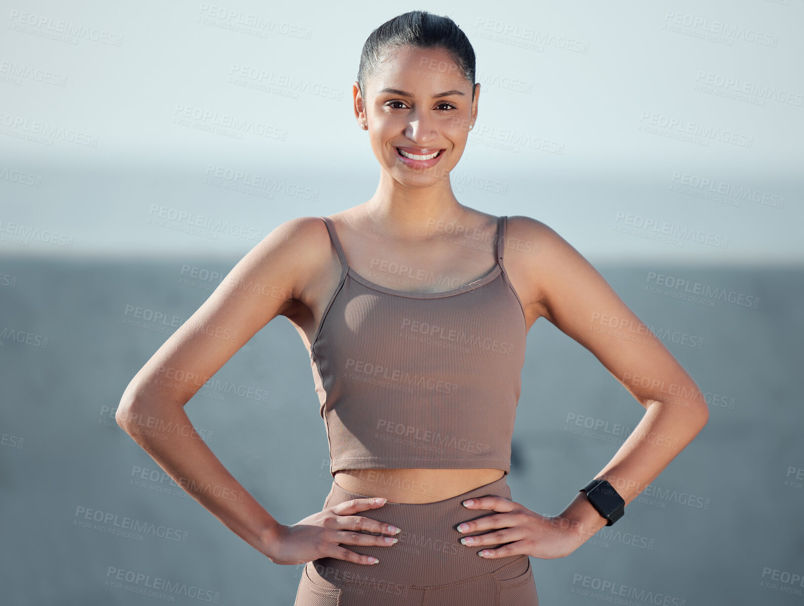 Buy stock photo Portrait of a sporty young woman standing with her hands on her hips while exercising outdoors