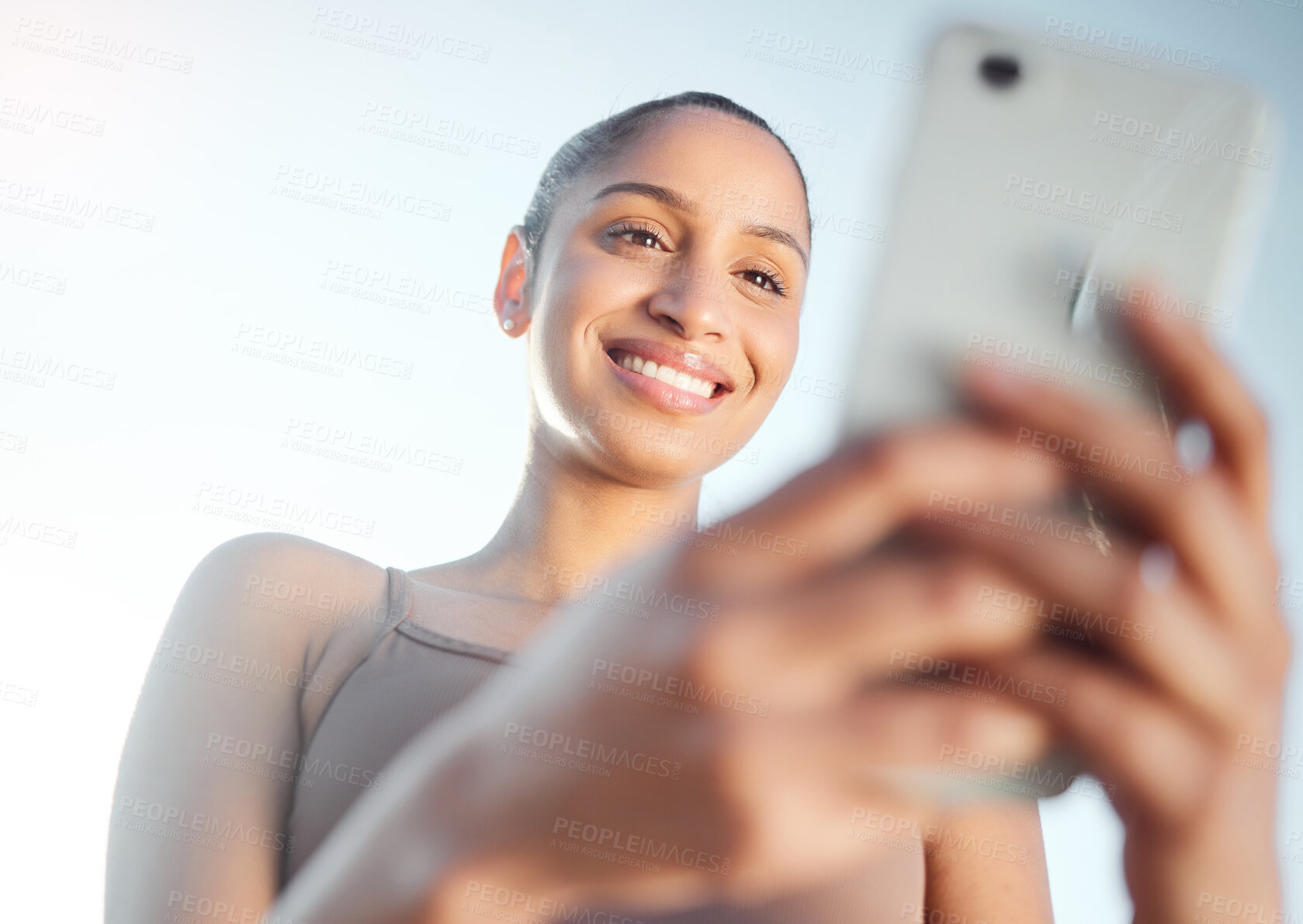 Buy stock photo Low angle shot of a sporty young woman using a cellphone while exercising outdoors