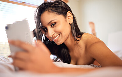 Buy stock photo Shot of a young woman using her cellphone while lying topless on her bed