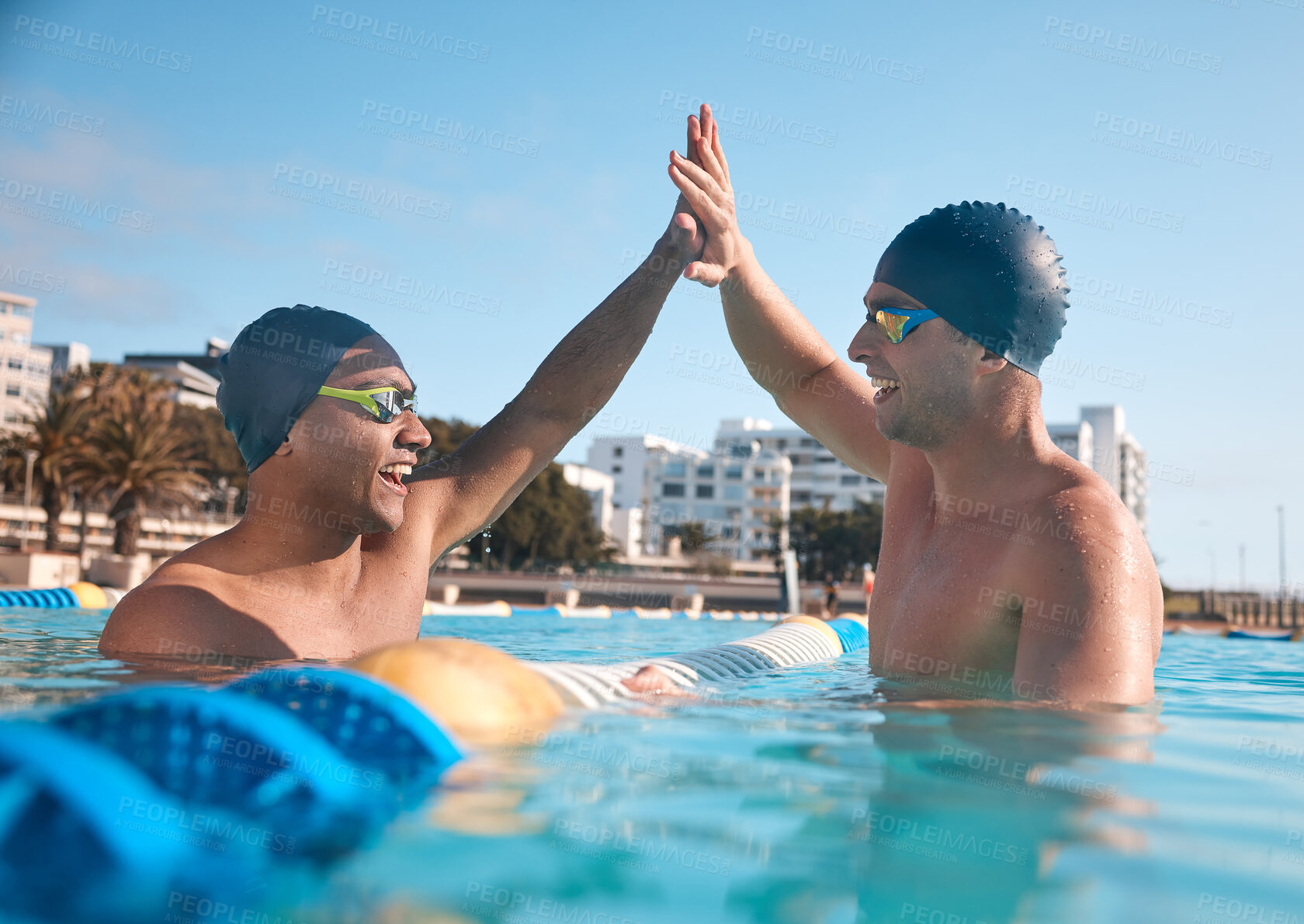 Buy stock photo Shot of two young men giving each other a high five while going for a swim in an olympic pool