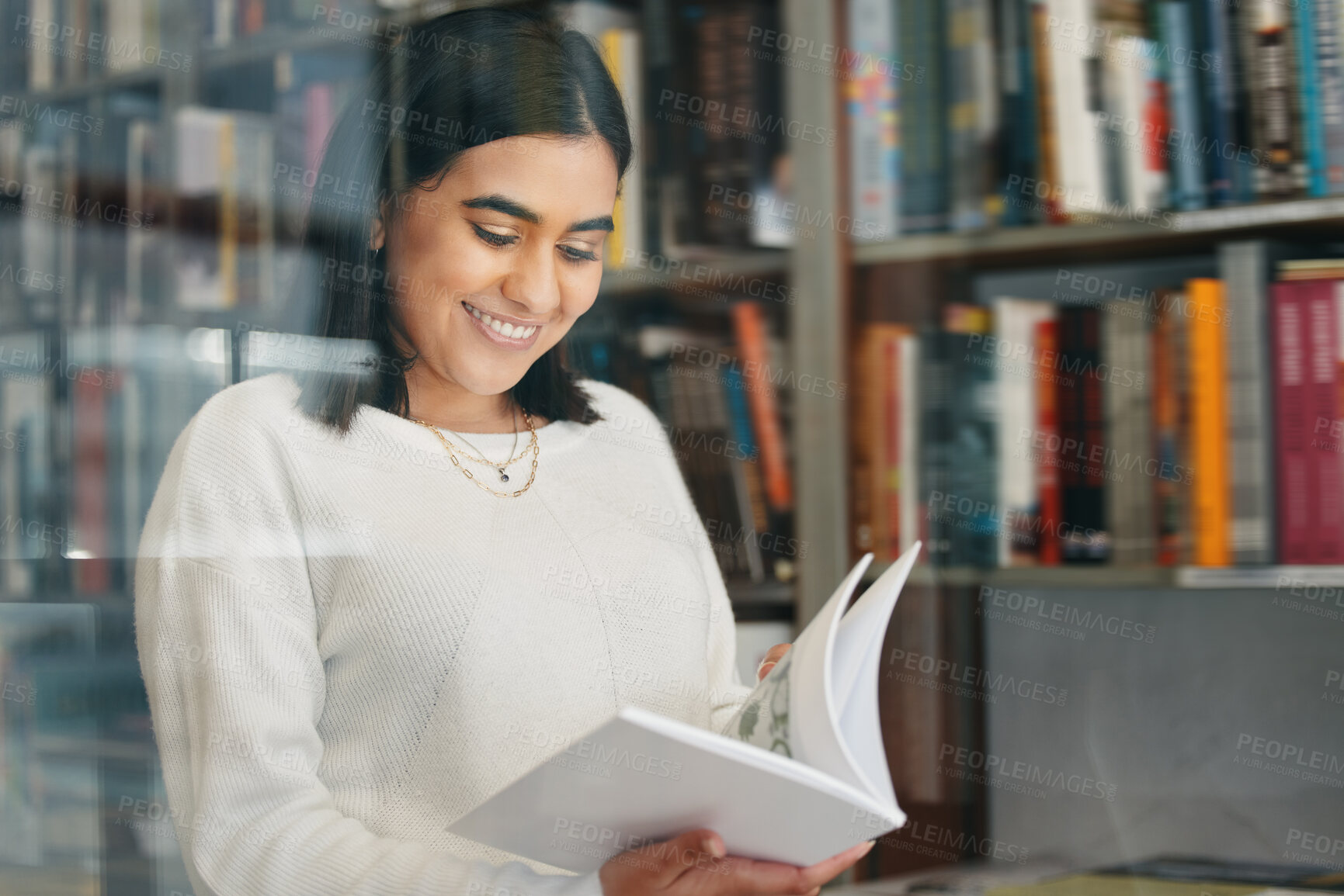 Buy stock photo Woman, student and reading in college library with smile for research, learning and education. Happy, female person, and university bookshelf with novel, literature or biography for studying