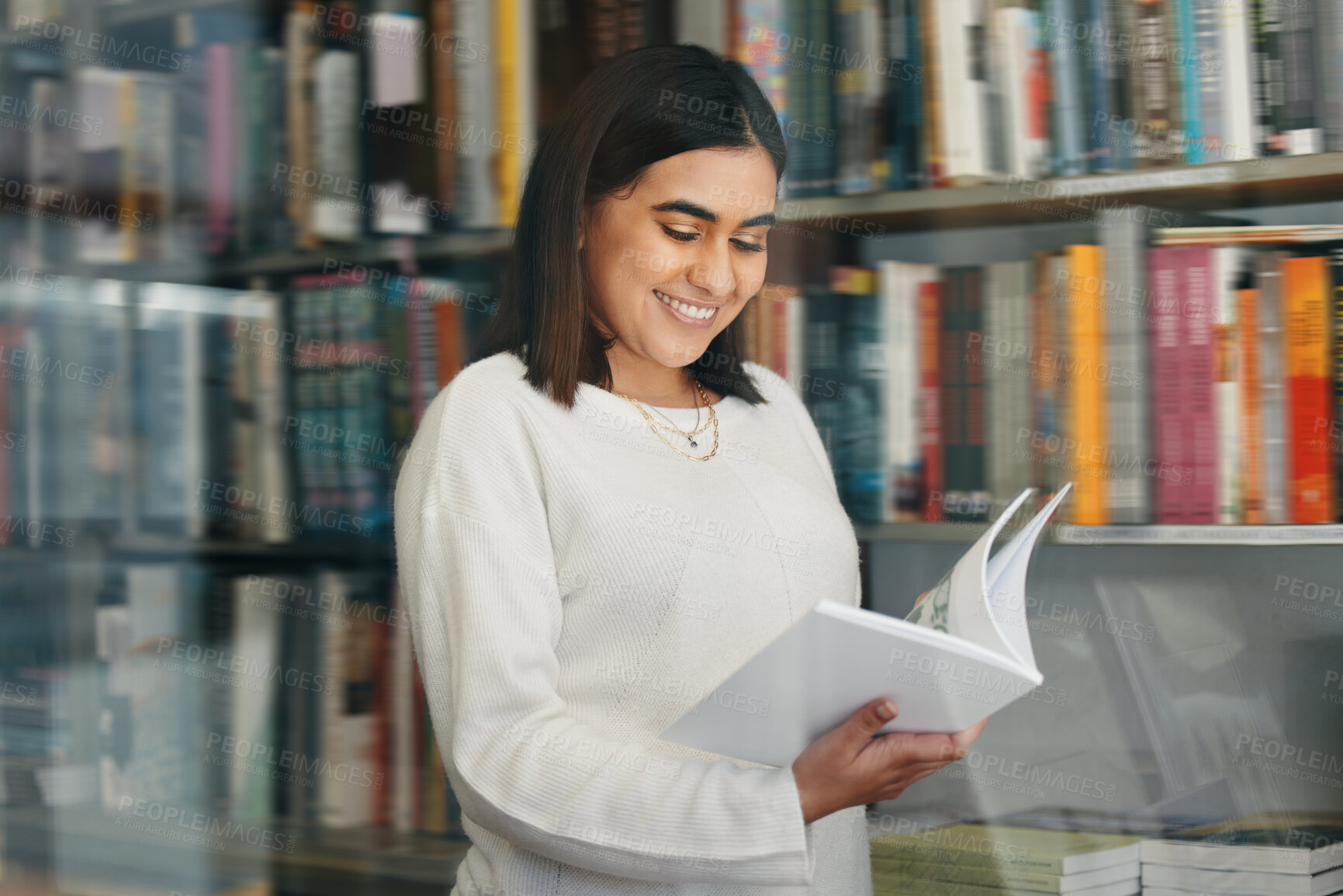 Buy stock photo Woman, student and reading in college library with smile for research, learning and education. Happy, female person, and university bookshelf with novel, literature or biography for studying