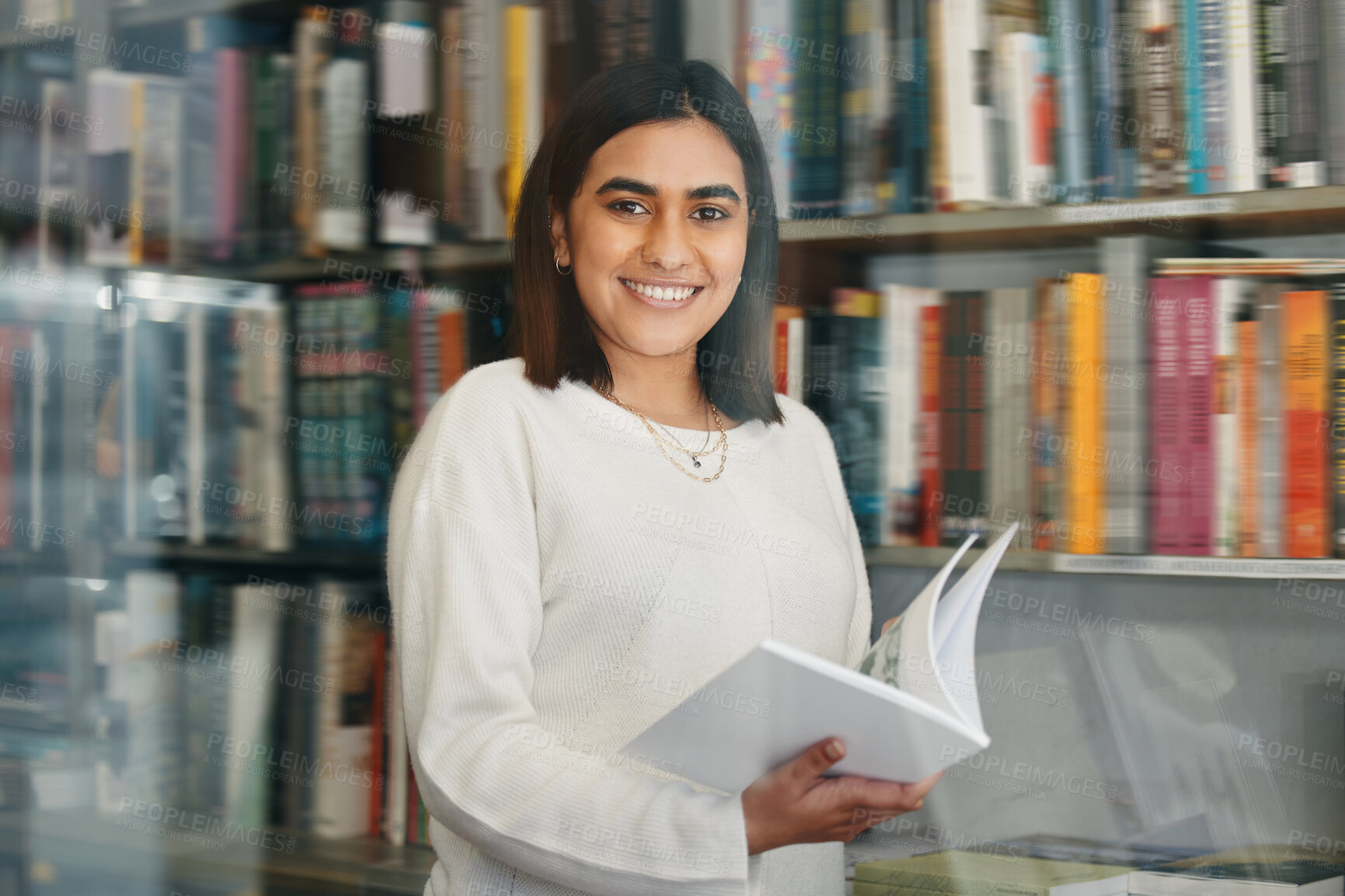 Buy stock photo Woman, student and portrait reading in college library with smile for research, learning and education. Happy, female person, and university bookshelf with novel, literature or biography for studying