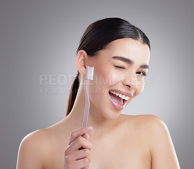 Buy stock photo Studio portrait of an attractive young woman brushing her teeth against a grey background