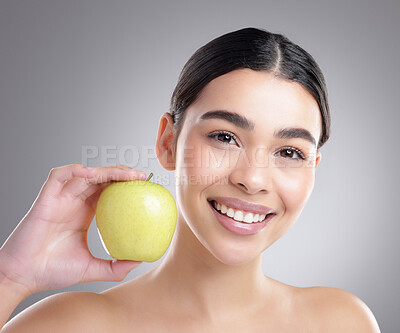 Buy stock photo Studio portrait of an attractive young woman posing with an apple against a grey background