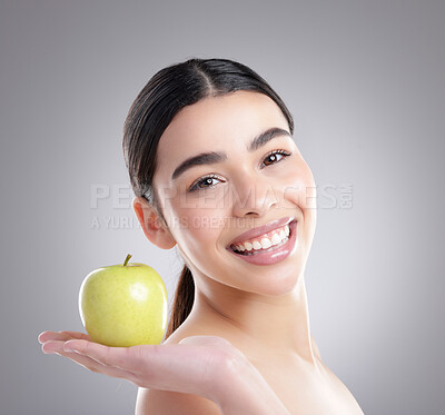 Buy stock photo Studio portrait of an attractive young woman posing with an apple against a grey background