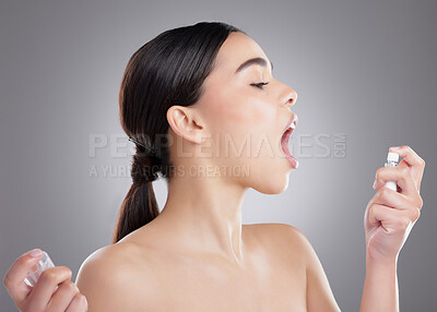 Buy stock photo Studio shot of an attractive young woman using breath freshener against a grey background