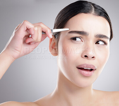 Buy stock photo Studio shot of an attractive young woman plucking her eyebrows against a grey background