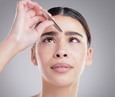 Buy stock photo Studio shot of an attractive young woman plucking her eyebrows against a grey background