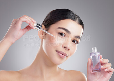 Buy stock photo Studio portrait of an attractive young woman applying facial serum against a grey background