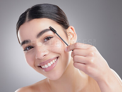 Buy stock photo Studio portrait of an attractive young woman apllying eyebrow makeup against a grey background