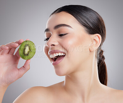 Buy stock photo Studio shot of an attractive young woman posing with half a kiwi against a grey background