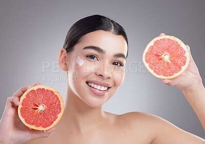 Buy stock photo Studio portrait of an attractive young woman posing with two halves of a grapefruit against a grey background