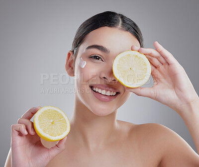 Buy stock photo Studio portrait of an attractive young woman posing with two halves of a lemon against a grey background